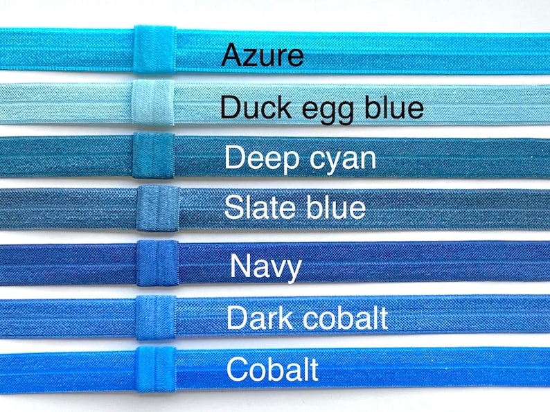 May include: Seven different shades of blue elastic hair ties, from light azure to dark cobalt. The hair ties are arranged in a row from lightest to darkest, with the color names written below each one.