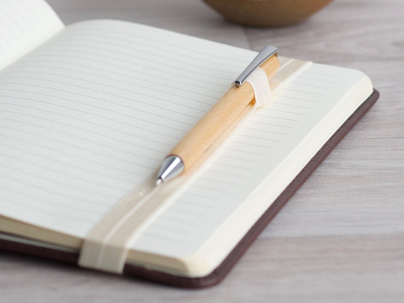 May include: A brown leather bound journal with a white ribbon bookmark and a wooden pen with a silver tip.
