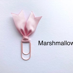 Może przedstawiać: R&oacute;żowa wstążka zawiązana wok&oacute;ł r&oacute;żowego złotego spinacza. Wstążka jest zawiązana w kokardkę. Tekst "Marshmallow" jest napisany pod spinaczem.