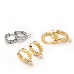 May include: A collection of six circular hoop earrings featuring a hinged closure mechanism and a small attached loop for charms. The set includes two silver-toned hoops and four gold-toned hoops, all with a smooth, polished metallic finish.