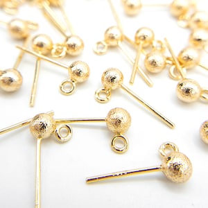 May include: A group of gold-toned earring findings with a textured ball and a loop at the top. The findings have a straight, thin wire extending from the ball.