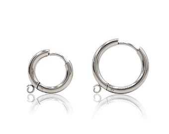 May include: Two silver-toned metal hoop earrings of different sizes, each featuring a hinged closure and a small circular loop attached to the bottom for hanging charms. The earrings have a polished, reflective finish and a simple, circular design.