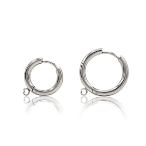 May include: Two silver hoop earrings with a hinged clasp and a small dangling loop. The earrings are made of metal and have a polished finish.