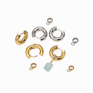Può includere: Una collezione di componenti per gioielli che include due paia di orecchini a cerchio spessi in tonalità oro e argento, quattro piccoli anellini di giunzione in metallo e un orecchino a cerchio dorato con un ciondolo in pietra azzurra.