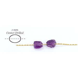 Peut inclure: Deux perles d'am&eacute;thyste violettes brutes enfil&eacute;es sur un fil dor&eacute; fin. Un sch&eacute;ma &agrave; gauche indique un trou perc&eacute; au centre de 1 mm. Les perles pr&eacute;sentent des surfaces irr&eacute;guli&egrave;res et dentel&eacute;es ainsi qu'une teinte violette profonde.