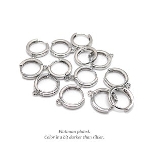Op de afbeelding: Een verzameling kleine, ronde, platina-geplateerde oorringen met bevestigingslusjes voor bedels. Het metaal heeft een gladde, reflecterende afwerking met een iets donkerdere tint dan zilver. Tekst: Platinum plated. Color is a bit darker than silver.