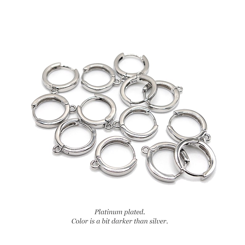 Op de afbeelding: Een verzameling kleine, ronde, platina-geplateerde oorringen met bevestigingslusjes voor bedels. Het metaal heeft een gladde, reflecterende afwerking met een iets donkerdere tint dan zilver. Tekst: Platinum plated. Color is a bit darker than silver.