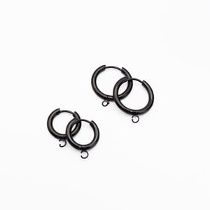 May include: Four black hoop earrings with a smooth, polished finish. Each circular earring features a small, integrated loop at the bottom, designed for attaching charms or pendants. The hoops have a hinged closure mechanism for secure fastening.