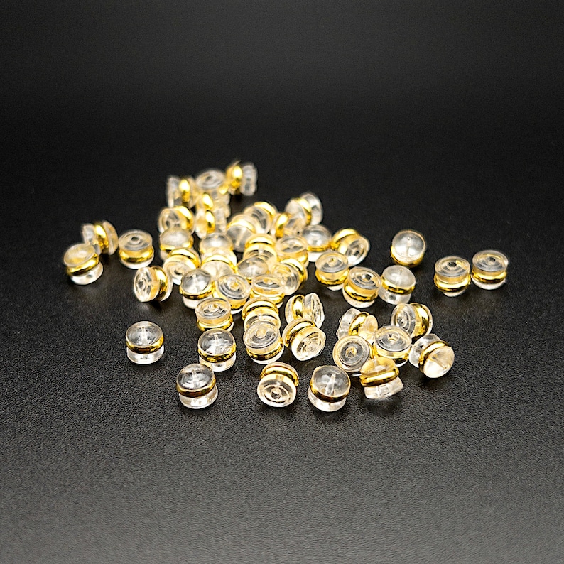 Puede incluir: Un mont&oacute;n de respaldos de pendientes de pl&aacute;stico transparente con anillos de metal dorado. Los respaldos est&aacute;n dise&ntilde;ados para ser usados con pendientes de bot&oacute;n.