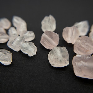 May include: A collection of small, translucent pink quartz crystals, also known as rose quartz, scattered on a black surface.