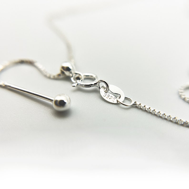 Puede incluir: Un collar de cadena de plata con un cierre de langosta y una peque&ntilde;a cuenta redonda en el extremo. La cadena est&aacute; marcada con "925", lo que indica que es de plata de ley.