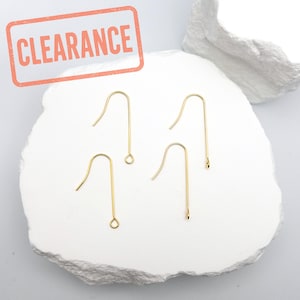 May include: Four gold earring hooks on a white surface. The hooks are made of metal and have a loop at the top.