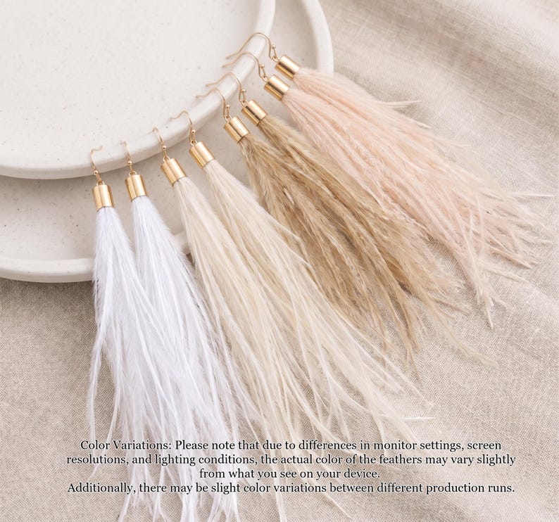 Puede incluir: Un conjunto de pendientes largos de plumas en varios colores, incluyendo blanco, crema, marr&oacute;n claro y rosa. Cada pendiente tiene una tapa y un gancho de metal dorado. Los pendientes se muestran en un plato de cer&aacute;mica blanco.