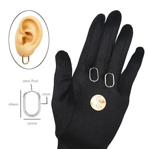 May include: A pair of silver oval hoop earrings with a 1 mm post and a 12 mm diameter. The earrings are shown on a black glove with a US penny for size comparison.