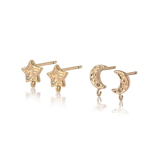 May include: Gold-colored stud earrings in star and crescent moon shapes. The star earrings have a textured surface and a small, clear gem. The moon earrings also have a textured surface and a small, clear gem. Both sets have a loop at the bottom.