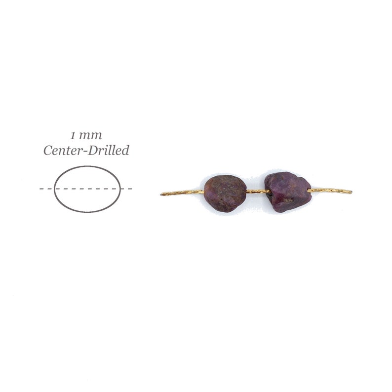 May include: Two raw, deep red ruby beads threaded on a thin gold wire. A diagram to the left shows an oval shape with a dashed line through the center, labeled 1 mm Center-Drilled, indicating the hole placement for these natural gemstone beads.