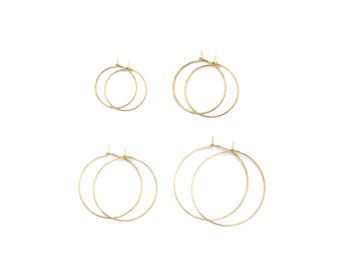 Peut inclure: Quatre boucles d'oreilles créoles dorées disposées en grille, dotées de fines montures circulaires en fil métallique avec des fermoirs à tige simples. L'ensemble comprend deux petites créoles en haut et deux plus grandes en bas, finition polie.