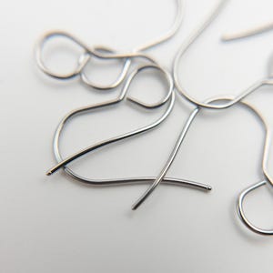 Peut inclure: Une collection de crochets de boucles d'oreilles en m&eacute;tal argent&eacute; pr&eacute;sentant un design en fil courb&eacute; avec une petite boucle sur le dessus pour la fixation et une extr&eacute;mit&eacute; arrondie sur la tige. Ces composants sont dispos&eacute;s en vrac.
