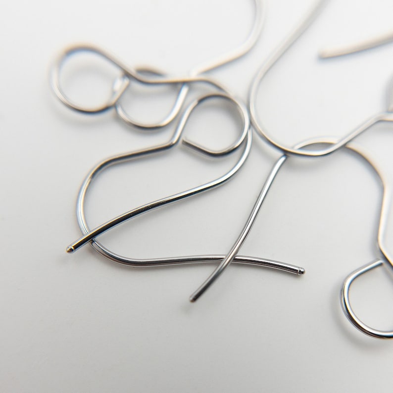 Peut inclure: Une collection de crochets de boucles d'oreilles en m&eacute;tal argent&eacute; pr&eacute;sentant un design en fil courb&eacute; avec une petite boucle sur le dessus pour la fixation et une extr&eacute;mit&eacute; arrondie sur la tige. Ces composants sont dispos&eacute;s en vrac.