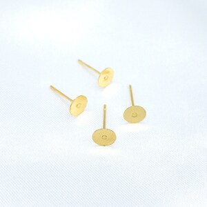 May include: Four gold-toned metal earring posts with flat circular pads. Each component features a thin, straight pin attached to the center of a small, round, textured disc, designed for attaching decorative elements to create stud earrings.