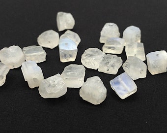 May include: A collection of small, translucent, off-white moonstone beads with irregular, raw-cut shapes. Each bead features a visible central drill hole, showcasing a smooth, polished texture on some surfaces and a rough, natural finish on others.