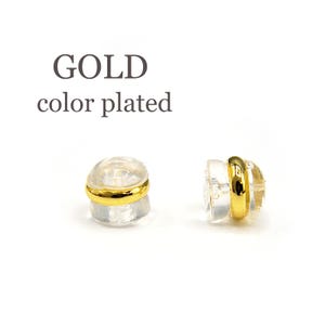 Puede incluir: Dos respaldos de pendientes chapados en oro, cada uno con un respaldo de pl&aacute;stico transparente y un anillo dorado alrededor del borde. El texto "GOLD color plated" es visible sobre los respaldos de los pendientes.
