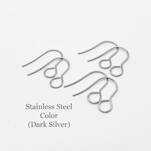 Peut inclure: Trois paires de crochets de boucles d'oreilles en acier inoxydable de couleur argent fonc&eacute;. Chaque crochet pr&eacute;sente un design en fil courb&eacute; avec une petite boucle circulaire &agrave; la base pour fixer des &eacute;l&eacute;ments. Le texte Stainless Steel Color (Dark Silver) est visible.