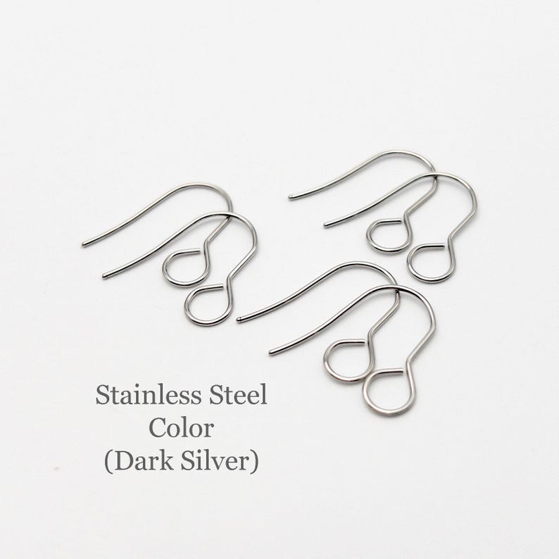Peut inclure: Trois paires de crochets de boucles d'oreilles en acier inoxydable de couleur argent fonc&eacute;. Chaque crochet pr&eacute;sente un design en fil courb&eacute; avec une petite boucle circulaire &agrave; la base pour fixer des &eacute;l&eacute;ments. Le texte Stainless Steel Color (Dark Silver) est visible.