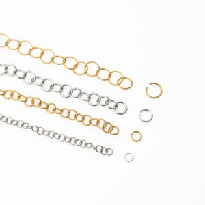 May include: Four lengths of metal chain in alternating gold and silver tones, each composed of interconnected circular links. To the right of the chains are four individual open jump rings, two in gold and two in silver, matching the chain colors.