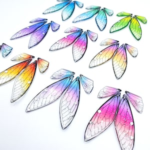 May include: Assortment of iridescent, glittery, and colorful butterfly wings. The wings are made of a translucent material and have a delicate, intricate design.