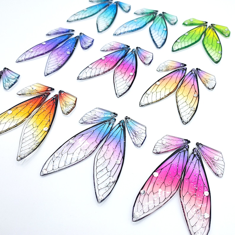 May include: Assortment of iridescent, glittery, and colorful butterfly wings. The wings are made of a translucent material and have a delicate, intricate design.