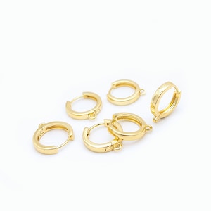 Op de afbeelding: Een verzameling van vijf kleine, gepolijste goudkleurige oorringen, elk voorzien van een scharniersluiting en een klein ge&iuml;ntegreerd oogje aan de onderkant voor het bevestigen van bedels of andere sieraden.