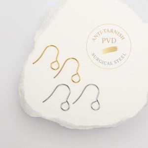 Peut inclure: Deux crochets de boucle d'oreille en m&eacute;tal dor&eacute; et deux en m&eacute;tal argent&eacute; avec un design en fil courb&eacute; et une boucle circulaire &agrave; la base. Un tampon circulaire indique Anti-Tarnish PVD Surgical Steel avec un motif de coup de pinceau dor&eacute;.