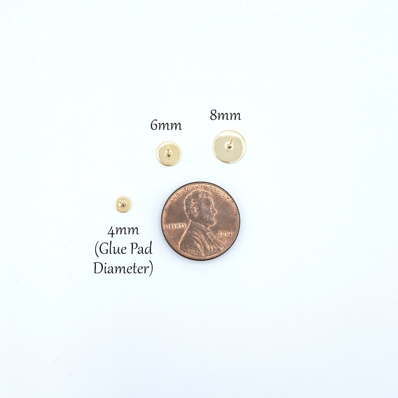 May include: Three gold-colored metal earring studs with flat circular glue pads. The studs are labeled with diameters of 4mm, 6mm, and 8mm. A copper-colored US penny is placed next to the studs for scale, showing the relative size of the components.