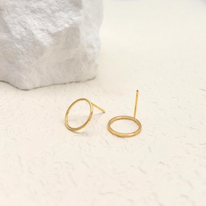 May include: A pair of gold-toned stud earrings, each featuring a thin, circular open hoop design. One earring is positioned flat, while the other stands upright, revealing the straight post and back attachment extending from the metal ring.