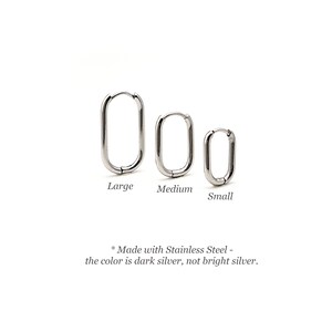 May include: Three stainless steel hoop earrings in different sizes: large, medium, and small. The earrings are oval shaped and have a dark silver finish.