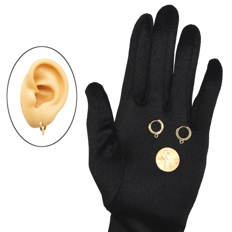 May include: Two small gold-toned hoop earrings, each featuring a tiny loop at the bottom for attaching charms. The hoops are shown next to a copper-colored penny for scale and are also depicted as worn on a beige-colored ear model.
