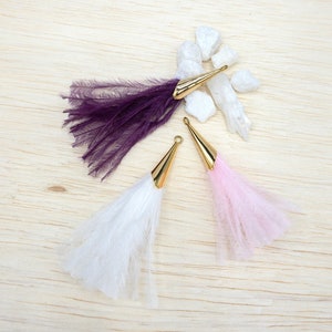 May include: Three feather tassels with gold metal tips. The tassels are purple, white, and pink.