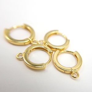 May include: Four gold-toned hoop earrings arranged in a cluster. Each hoop features a smooth, polished finish and a hinged closure mechanism. Two of the hoops include a small, circular loop attached to the bottom edge for hanging additional charms.