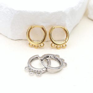May include: Two pairs of hoop earrings with three jump rings hanging from each hoop. One pair is gold and the other is silver.