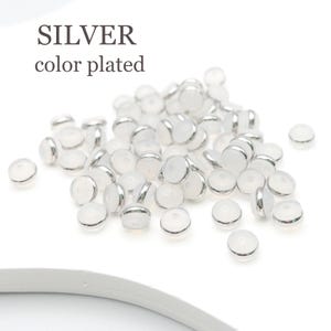 Puede incluir: Un mont&oacute;n de cuentas de vidrio blanco con bordes plateados. Las cuentas son redondas y tienen una superficie plana. El texto "SILVER color plated" es visible en la imagen.