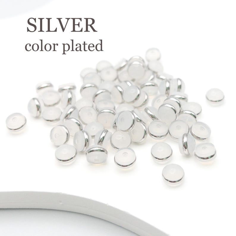Puede incluir: Un mont&oacute;n de cuentas de vidrio blanco con bordes plateados. Las cuentas son redondas y tienen una superficie plana. El texto "SILVER color plated" es visible en la imagen.