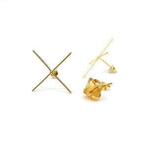 May include: A pair of gold earrings with a raw, orange-brown gemstone set in each. The earrings are made with a simple, minimalist design.