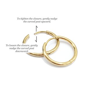 May include: Two polished gold hoop earrings with a hinged closure. Text instructions are included: To tighten the closure, gently nudge the curved post upward. To loosen the closure, gently nudge the curved post downward. The hoops are circular.