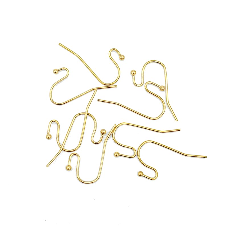 May include: A collection of gold-toned metal earring hooks, each featuring a curved wire design with a small decorative ball at the end. These jewelry components are arranged in a scattered pattern, showcasing the smooth finish and consistent shape.