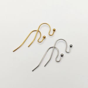 May include: Two ear cuffs, one in a gold tone and one in a silver tone. Each ear cuff features a curved wire design with a small ball at the end of the hook, designed to wrap around the ear cartilage. The metal surfaces are smooth and polished.