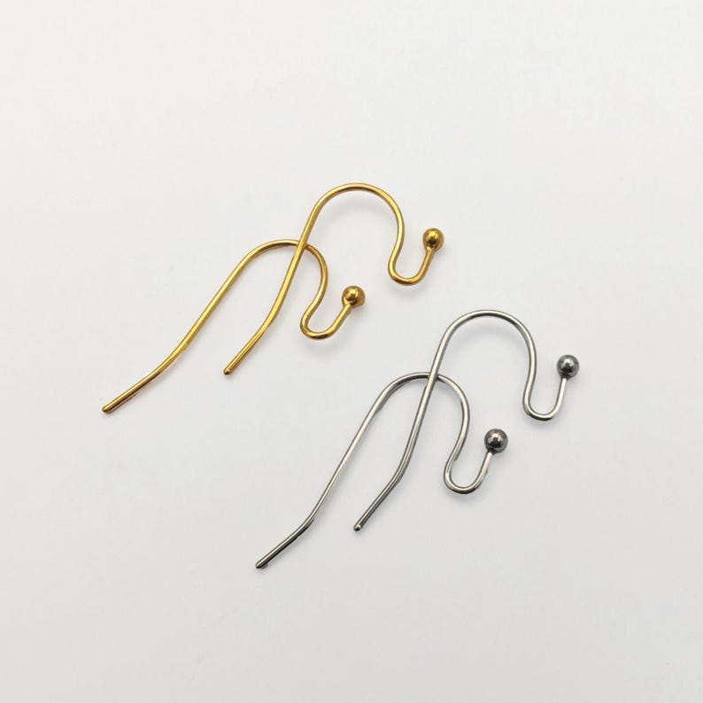 May include: Two ear cuffs, one in a gold tone and one in a silver tone. Each ear cuff features a curved wire design with a small ball at the end of the hook, designed to wrap around the ear cartilage. The metal surfaces are smooth and polished.