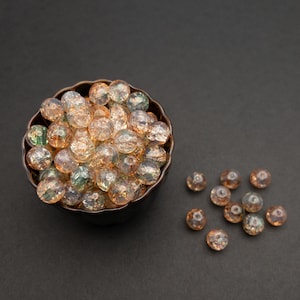 May include: A bowl filled with iridescent glass beads in shades of green, brown, and clear. The beads are scattered around the bowl on a black surface.