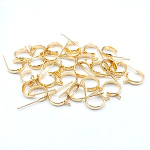 May include: A pile of gold-toned earring hoops with a small loop at the top and a straight pin on the bottom.