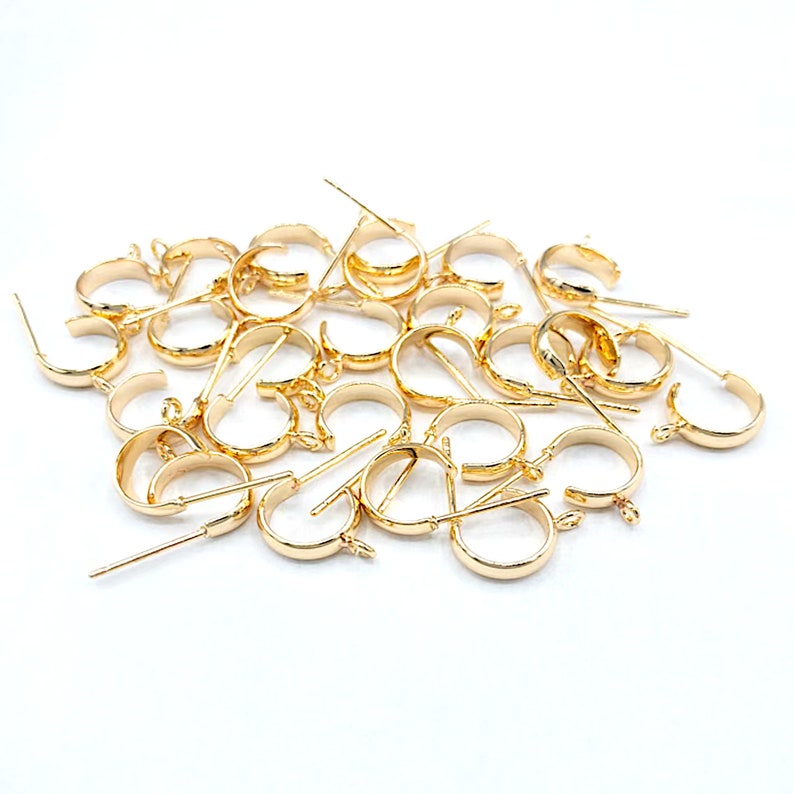 May include: A pile of gold-toned earring hoops with a small loop at the top and a straight pin on the bottom.